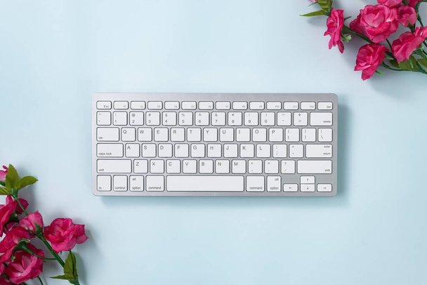 Λευκό φορητό Πληκτρολόγιο Πληκτρολόγιο Κλειδιά ή Πληκτρολόγιο Κουμπί και τριαντάφυλλο Λουλούδι στην επάνω δεξιά και κάτω αριστερή γωνία σε μπλε παστέλ μινιμαλιστικό φόντο - Φωτογραφία, εικόνα