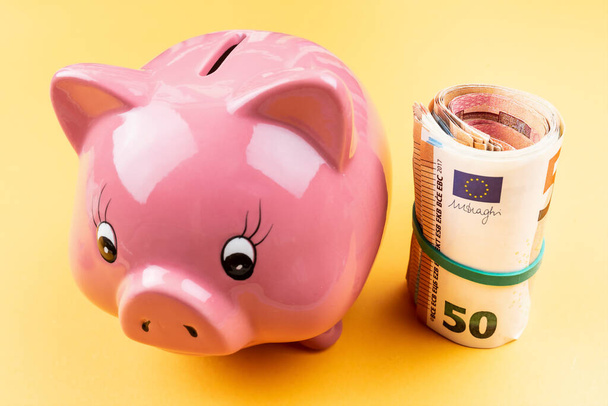 άποψη υψηλής γωνίας του roll χρήματα με λαστιχάκι δίπλα στο ροζ κουμπαρά - Φωτογραφία, εικόνα