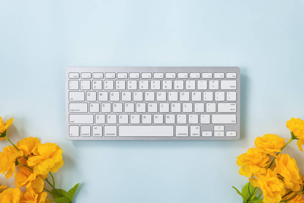 Teclas portáteis brancas do teclado do computador ou botão do teclado e flor amarela na parte inferior no fundo minimalista azul Pastel - Foto, Imagem