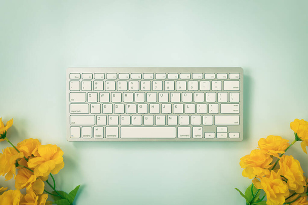Teclas de teclado de computador portátil branco ou botão de teclado e flor amarela na parte inferior em fundo minimalista azul pastel em tom vintage - Foto, Imagem
