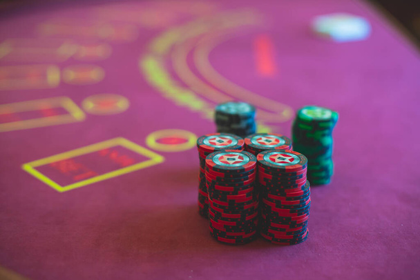 A close-up vibrant image of multicolored casino table with roulette in motion, with casino chips. the hand of croupier, mone and a group of gambling rich wealthy people in a backgroun - Photo, image