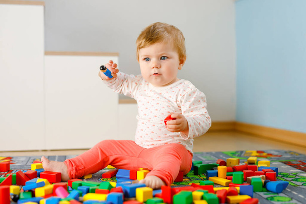 教育用のおもちゃで遊んでいる愛らしい赤ちゃんの女の子。国内の部屋でカラフルな異なる木製のブロックで楽しい時間を過ごしている幸せな健康な子供。赤ちゃんの学習の色と形 - 写真・画像