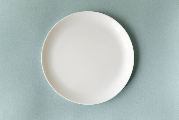 Empty white plate on a blue background. Horizontal orientation. Top view. Copy space. - Foto, afbeelding