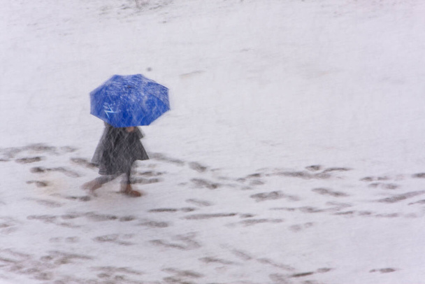 Θολή εικόνα - ένα θηλυκό περπάτημα κάτω από ομπρέλα σε βαριά χιονόπτωση - Φωτογραφία, εικόνα