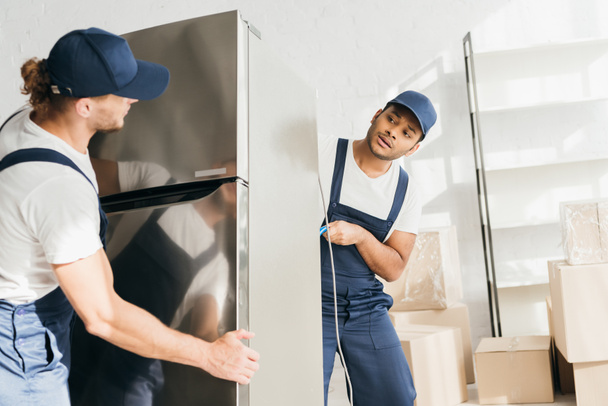 Indian mover looking at coworker while moving fridge in apartment  - Photo, Image