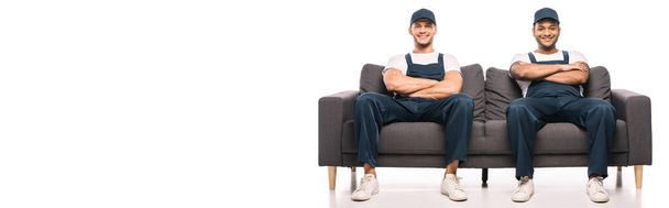 full length of cheerful multicultural movers sitting on sofa with crossed arms and smiling on while, banner - Фото, зображення