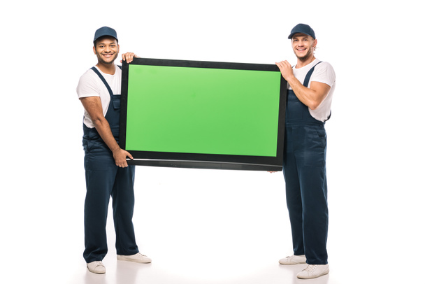 plná délka šťastný multikulturní stěhováci nesoucí plazmovou televizi se zelenou obrazovkou na bílém - Fotografie, Obrázek