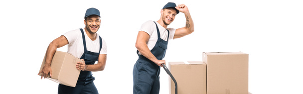 excited multicultural movers in uniform and caps near hand truck with carton boxes on white, banner - Foto, imagen