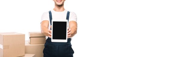 partial view of cheerful mover in uniform holding digital tablet with blank screen near carton boxes isolated on white, banner - Фото, изображение
