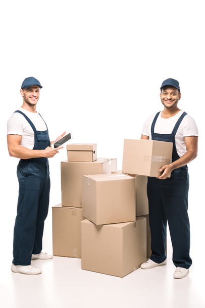 full length of cheerful worker holding digital tablet and standing with indian mover near boxes on white - Photo, Image