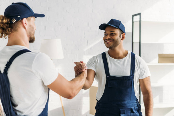 happy multiethnic workers shaking hands in apartment  - Photo, Image