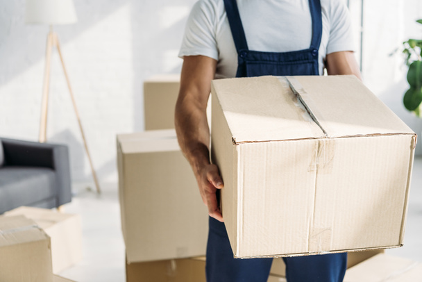 partial view of mover in uniform holding carton box in apartment  - Foto, immagini