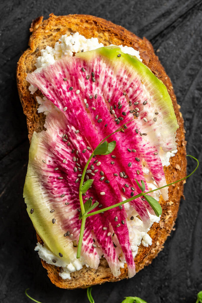 Bruschetta with goat cheese, watermelon radish, microgreen and chia seeds, vertical image. Food recipe background. Close up. - Photo, Image