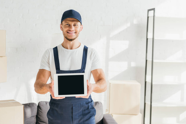 cheerful mover in uniform holding digital tablet with blank screen in apartment  - Fotoğraf, Görsel
