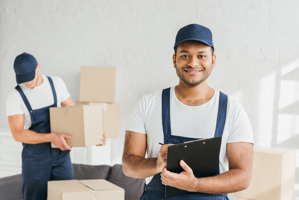 cheerful indian worker holding clipboard near coworker on blurred background  - Photo, Image