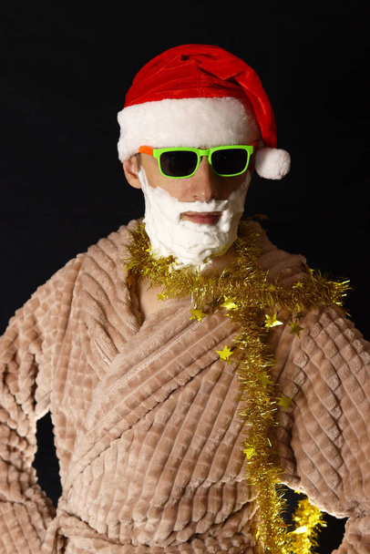 Κακός Άγιος Βασίλης με γενειάδα αφρού ξυρίσματος σε μια ρόμπα σε μαύρο φόντο - Φωτογραφία, εικόνα