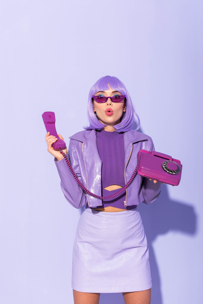 shocked young woman dressed in doll style with retro telephone on violet colorful background - Photo, Image