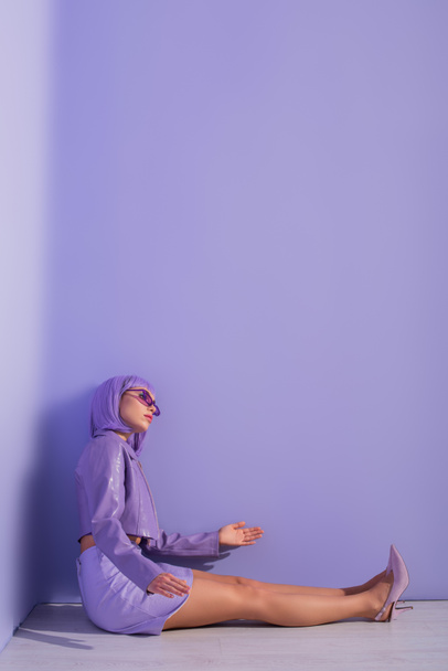Bebek gibi giyinmiş genç bir kadın menekşe renkli arka planda yerde oturuyor. - Fotoğraf, Görsel