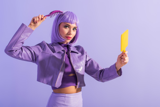 mujer joven vestida con estilo de muñeca con cepillo de pelo y espejo sobre fondo de color violeta - Foto, imagen