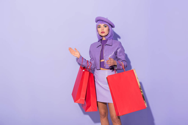 mujer joven vestida con estilo de muñeca con bolsas de compras rojas sobre fondo de color violeta - Foto, imagen
