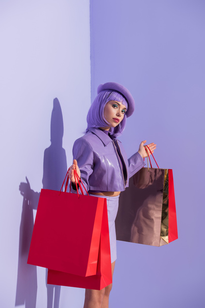 mujer joven vestida con estilo de muñeca con bolsas de compras rojas sobre fondo de color violeta - Foto, imagen