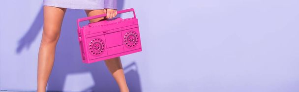 紫のカラフルな背景にピンクのレトロテープレコーダーでポーズ人形のスタイルで身に着けている若い女性のクロップドビュー、バナー - 写真・画像
