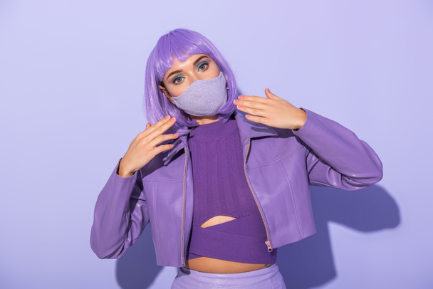 Nukkeihin pukeutunut nuori nainen lääketieteellisessä naamiossa diskopallolla violetilla värikkäällä taustalla - Valokuva, kuva