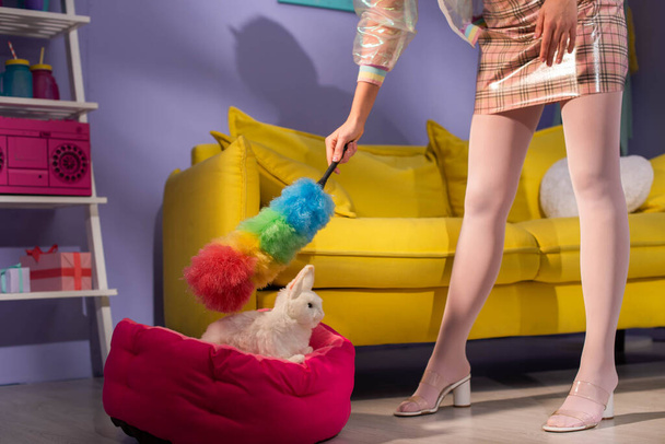 обрізаний вид на молоду жінку, позуючи як ляльку з пилкою біля іграшкового кролика вдома
 - Фото, зображення