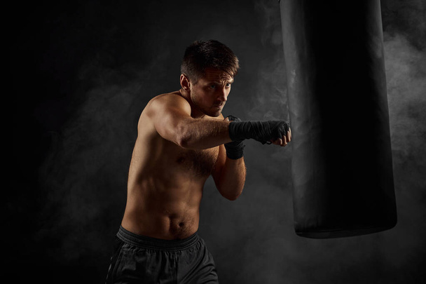 Male boxer punching in boxing bag on black background - Fotoğraf, Görsel