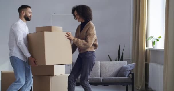 Multi-ethnic couple curly girl and Caucasian handsome man bring heavy cardboard boxes together move to new house buying apartment receive delivery clap hands give five collaboration support concept - Footage, Video