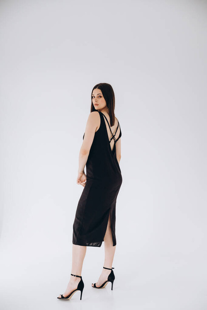 24.06.2020 Vinnitsa, Ukraine: pretty woman with dark long hair posing for a photo on a cyclorama in a photo studio dressed in a black dress with open shoulders - Foto, imagen