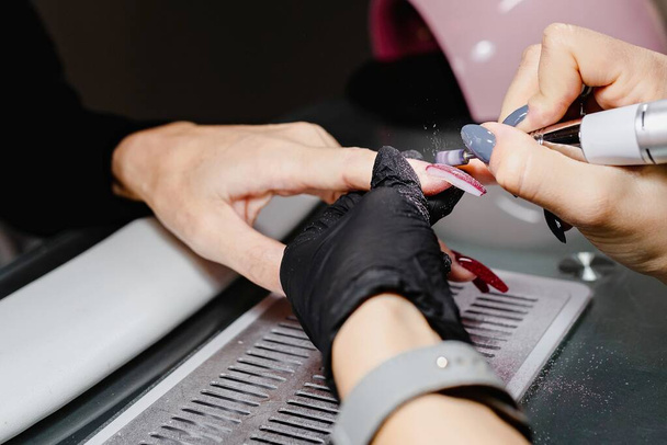  Close up unrecognizable woman hands. Manicurist removing gel from client's nails with milling cutter. Beauty, professional, process concept. - Photo, image