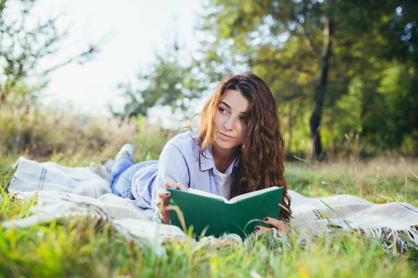 Nostalgic teenage girl is sitting in the park and reading book - Foto, imagen