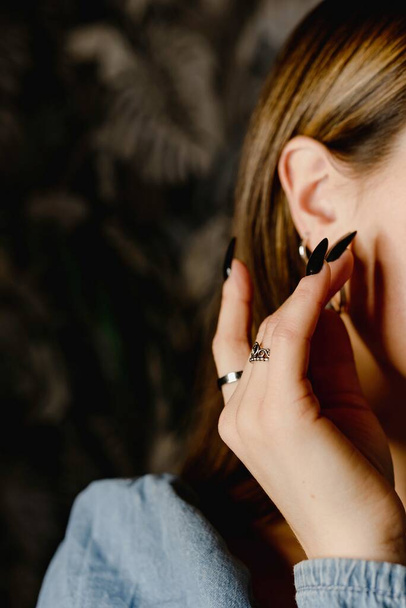 Unerkennbare vertikale Nahaufnahme Frauenhand mit schwarzem Nagellack, der Hals und Ohrringe berührt. Schönheitskonzept. - Foto, Bild
