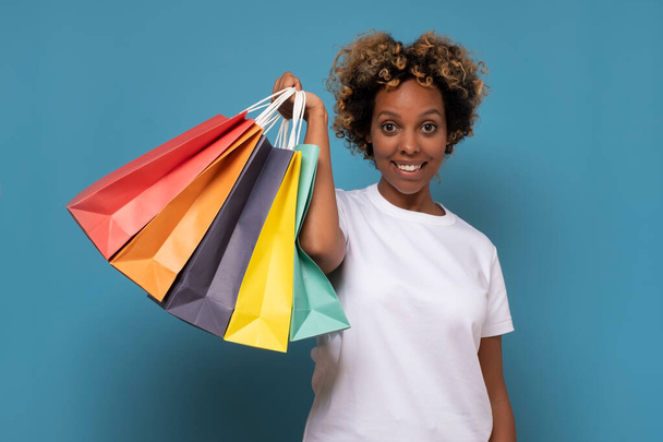 Piękna młoda Afrykanka z kolorowymi torbami na zakupy jest podekscytowana swoimi zakupami. - Zdjęcie, obraz
