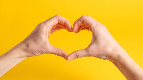 Zwei Hände formen mit den Fingern eine Herzform. Herzförmige Hände auf gelbem Hintergrund. Hände machen ein Herz - Foto, Bild