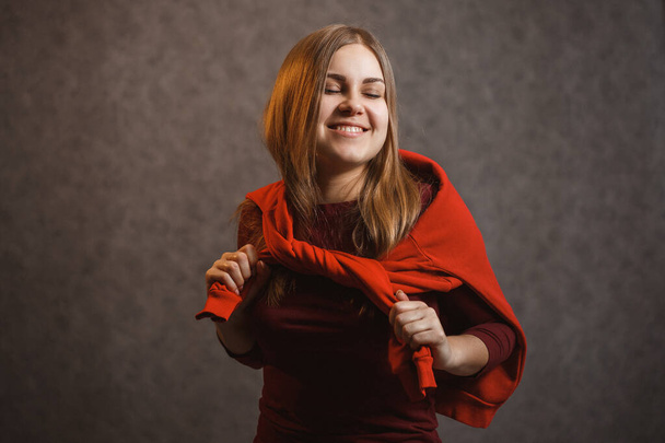 Girl tries on a red sweater on a gray background - 写真・画像