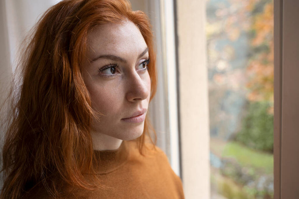Молодая обеспокоенная женщина смотрит в окно - Фото, изображение