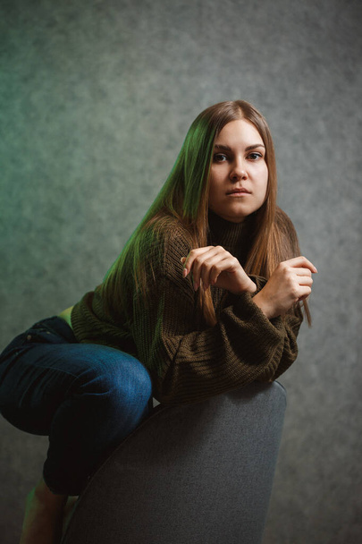 Girl in a green sweater and jeans on a gray chair and smiling - Foto, Bild