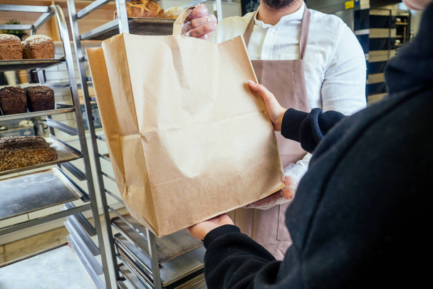 Cheerful baker delivering bread to client in store - Foto, imagen