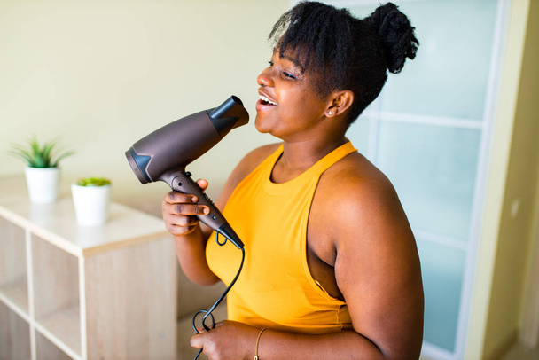beautiful afro woman drying hairs and singing like a microphone - Foto, afbeelding