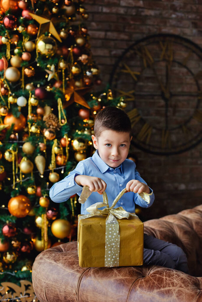 Cute little boy about five years old with a gift in a decorated Christmas room with a Christmas tree. Opens a gift. - Foto, immagini