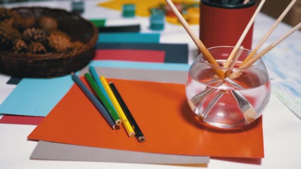 Az asztalon véletlenszerűen elrendezett avokarel festékek, ceruzák, ecsetek, színes papír - Felvétel, videó