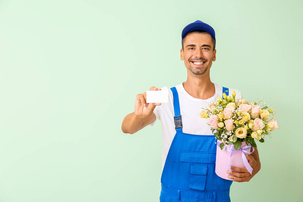 Delivery man with bouquet of flowers and business card on color background - Photo, image