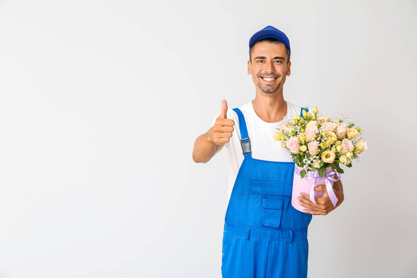 Delivery man with bouquet of flowers showing thumb-up on light background - Photo, Image