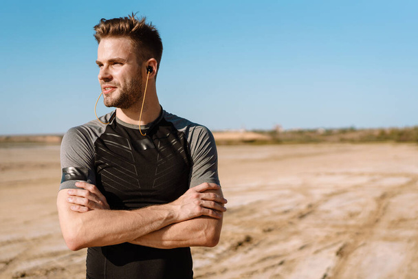 Portrait of a fit sportsman listening to music with earphones while standing at the beach - Foto, imagen
