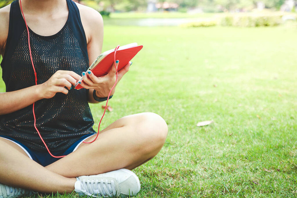 Hermosa adolescente asiática le gusta hacer ejercicio Use auriculares, sostenga una tableta en el parque. - Foto, imagen