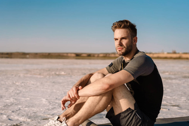 Atractivo joven deportista sentado en el lago de sal, descansando - Foto, imagen