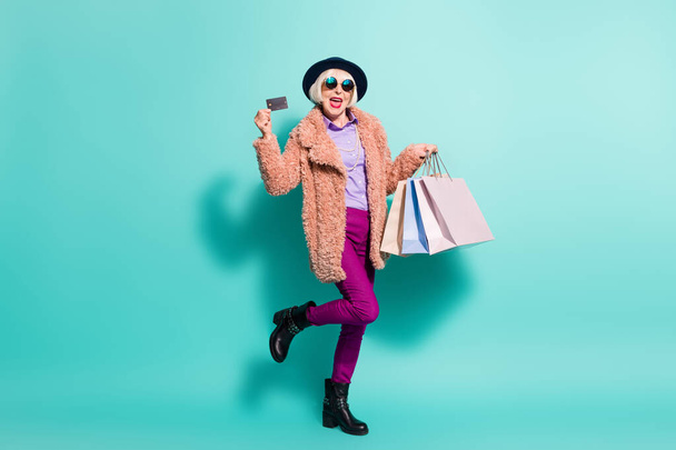 Photo of shopaholic senior lady wear retro jacket headwear eyeglasses holding bargains credit card isolated teal color background - Fotó, kép