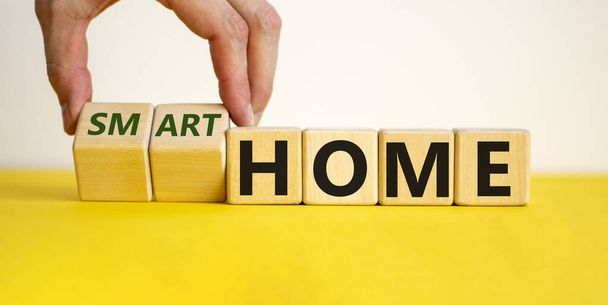 Normal or smart home . Hand turns cubes and changes the words 'home' to 'smart home'. Beautiful yellow table, white background. Business and smart home concept. Copy space. - Photo, image